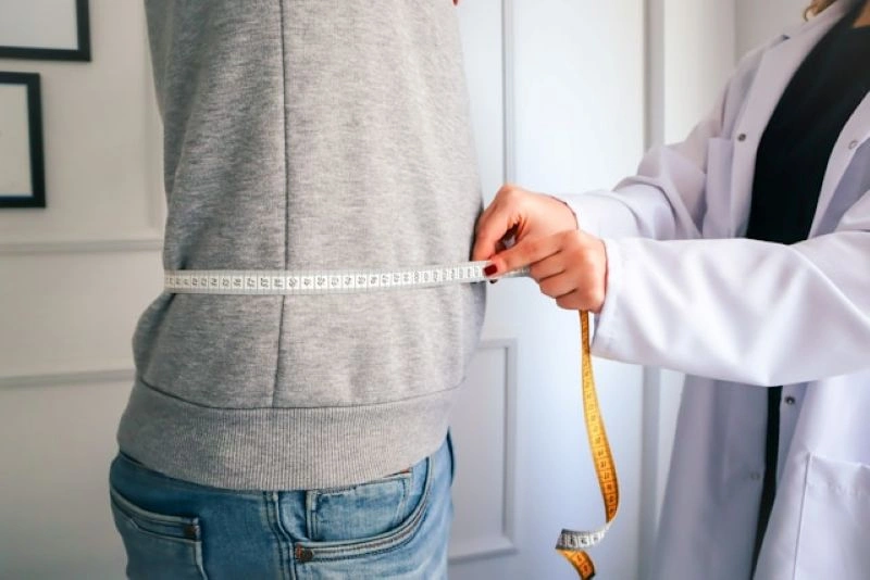 Close-up of a person’s midsection with a measuring tape, illustrating body image concerns related to anorexia nervosa vs bulimia nervosa.