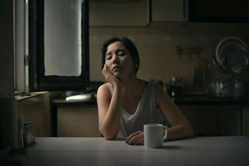 Young woman resting her head on her arms at a table, representing fatigue and emotional distress in anorexia nervosa vs bulimia nervosa