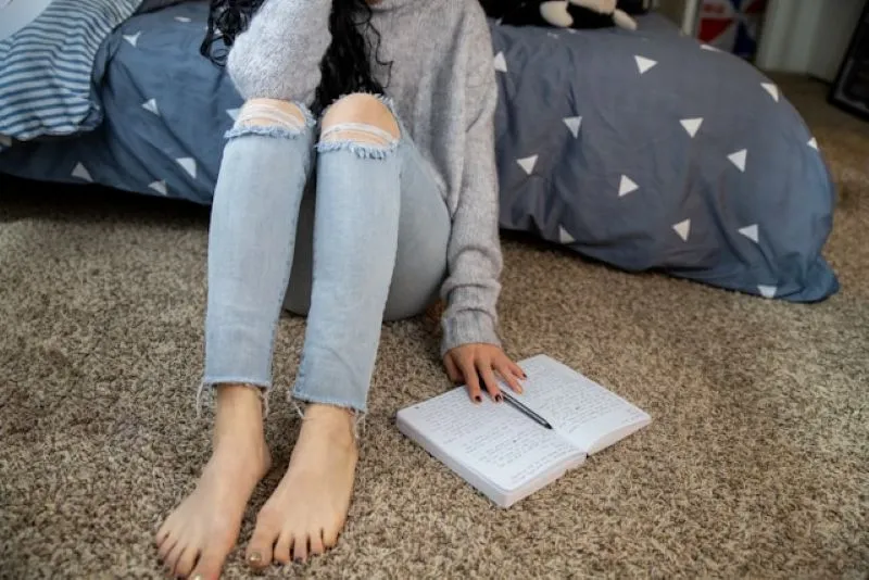 A person sitting on the floor next to a notebook, appearing reflective or journaling, highlighting mental health support from pmdd specialists.