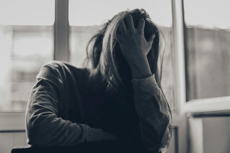 Person sitting by a window with head in hands, appearing withdrawn and overwhelmed, illustrating early signs depression is getting worse.