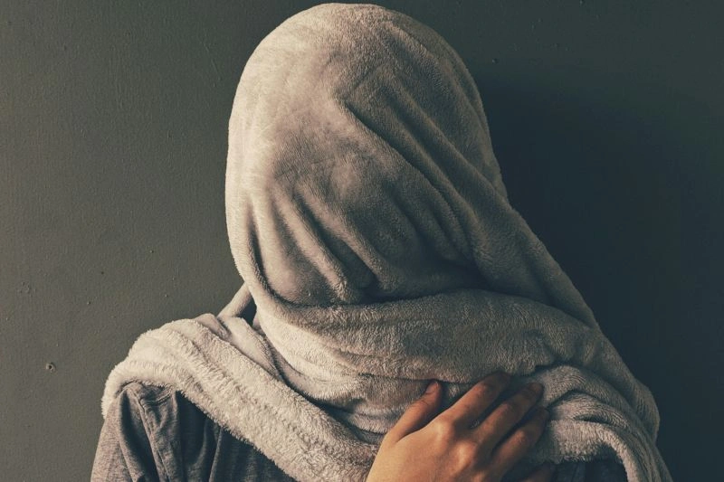 Individual with head and face covered by a blanket or fabric, holding themselves tightly in distress, reflecting signs depression is getting worse.