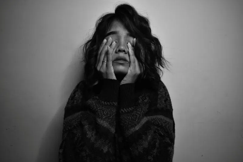Black-and-white portrait of a woman covering her face with her hands in emotional distress, symbolizing overwhelming feelings associated with chronic emptiness.