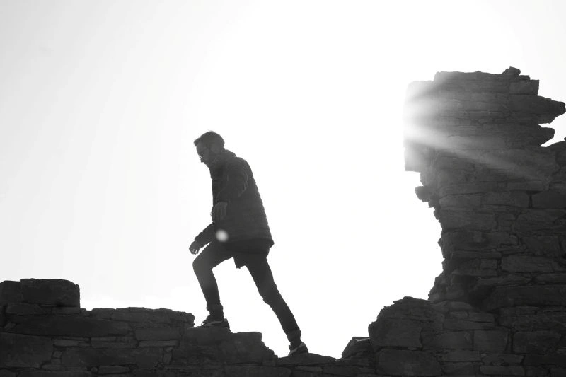 Fear of failure represented by a person carefully walking across rocky terrain with a challenging path ahead.