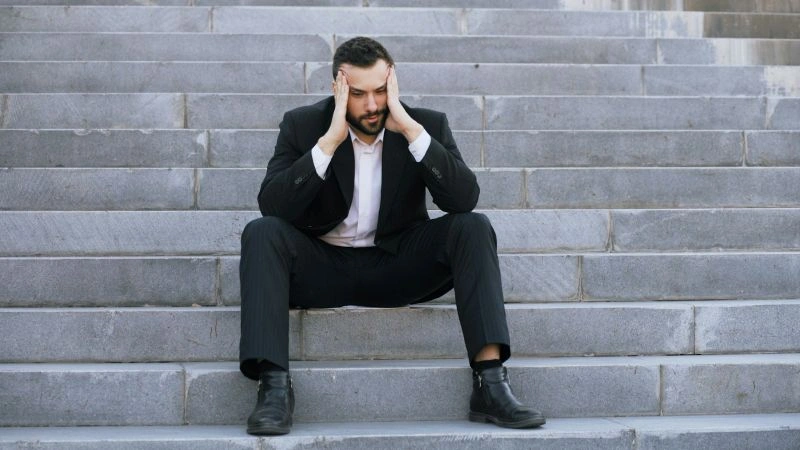Fear of failure depicted by a stressed professional sitting alone on steps and feeling overwhelmed by challenges.