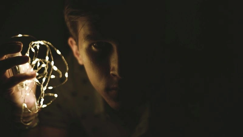 Hypervigilance in anxiety illustrated by a person holding a light in a dark room, representing searching for safety and staying alert.