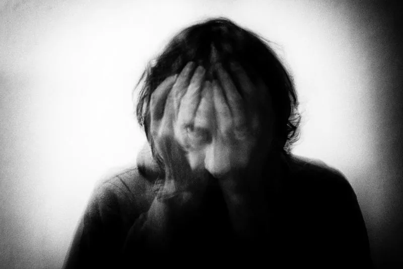 Blurred, high-contrast image of a person covering their face, conveying emotional overwhelm and detachment linked to emotional numbness.