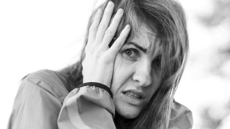 Black-and-white portrait of a woman holding the side of her head with a tense expression, representing overwhelming inner struggle and emotional numbness.
