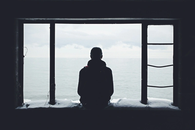 Person sitting alone and looking out toward the sea, representing isolation and low mood in discussions of depression vs sadness.