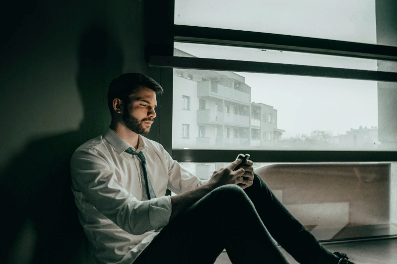 Man sitting alone by a window with a withdrawn expression, reflecting emotional distress that may raise questions about depression vs sadness.