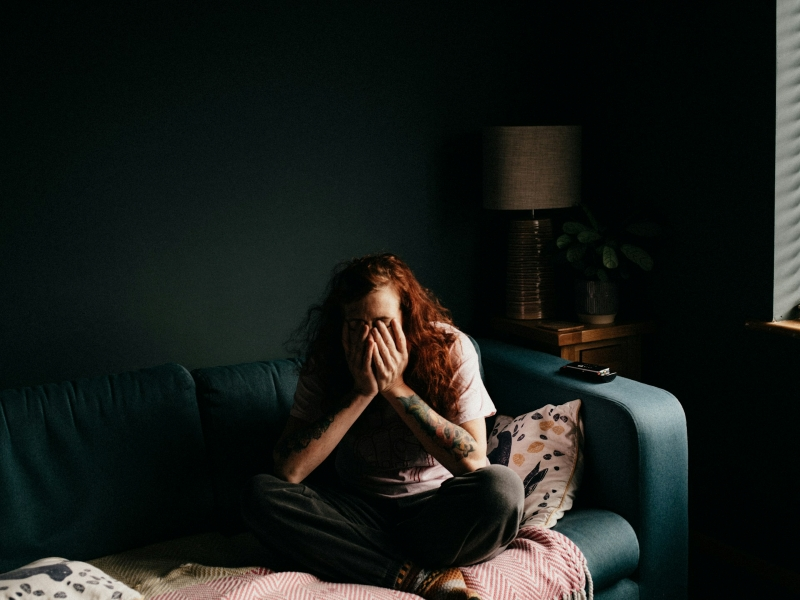 Woman sitting on a sofa with her face in her hands, reflecting the emotional distress often experienced when learning how to heal anxiety without medication.