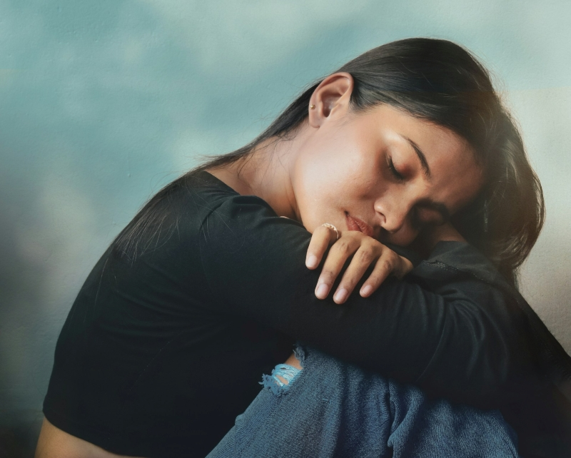 Young woman sitting with her knees pulled close and eyes closed, showing emotional exhaustion while exploring how to heal anxiety without medication.