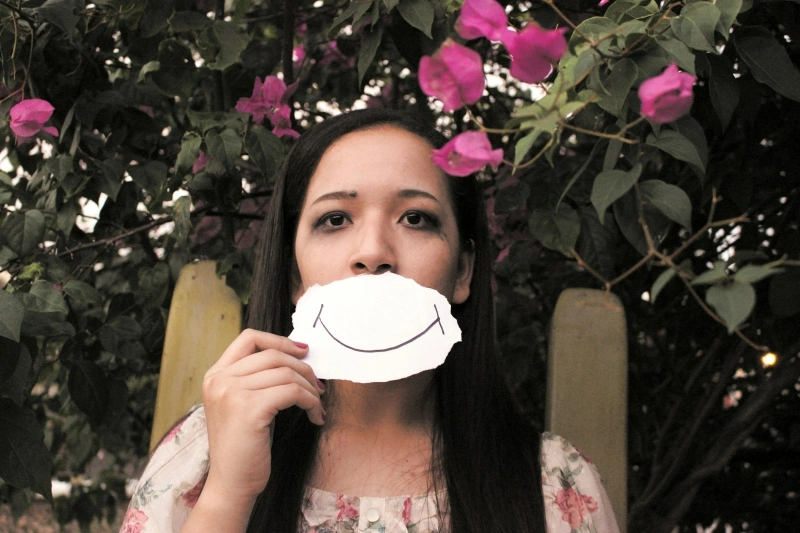 Teen girl holding a paper smile in front of her face, symbolizing hidden emotional distress and the need for depression treatment for teenager.