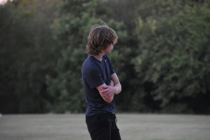 Teenage boy standing alone outdoors with a withdrawn posture, representing isolation and low mood associated with the need for depression treatment for teenager.